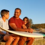 dad and kids with a surf board