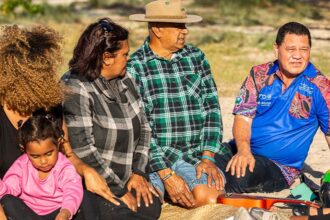 A group of Aboriginal and Torres Strait Island people are sitting in the Australian bush looking towards a Diabetes Australia First Nations health worker while talking.