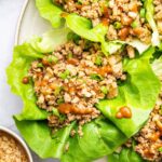 Ground chicken lettuce wraps served on a plate with a peanut sauce drizzle and fresh green onions.