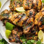 Cooked cilantro lime chicken thighs served on a plate topped with fresh cilantro and lime wedges.
