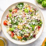 Greek quinoa salad in a tan serving bowl topped with crumbled feta cheese.