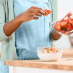 woman adding fruit to yogurt