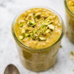 A jar of pistachio overnight oats topped with chopped pistachios.